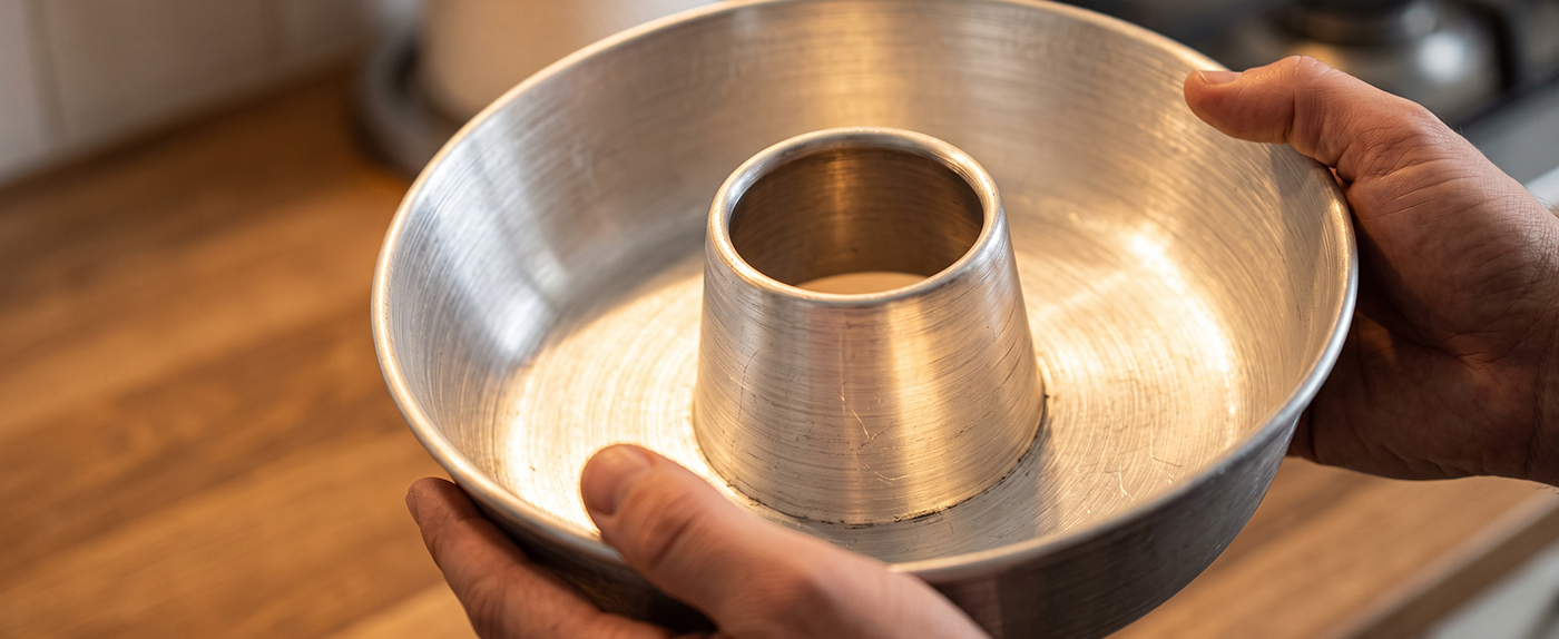 Hands holding a Globe Rocket aluminum ring cake pan, showing its bare metal construction