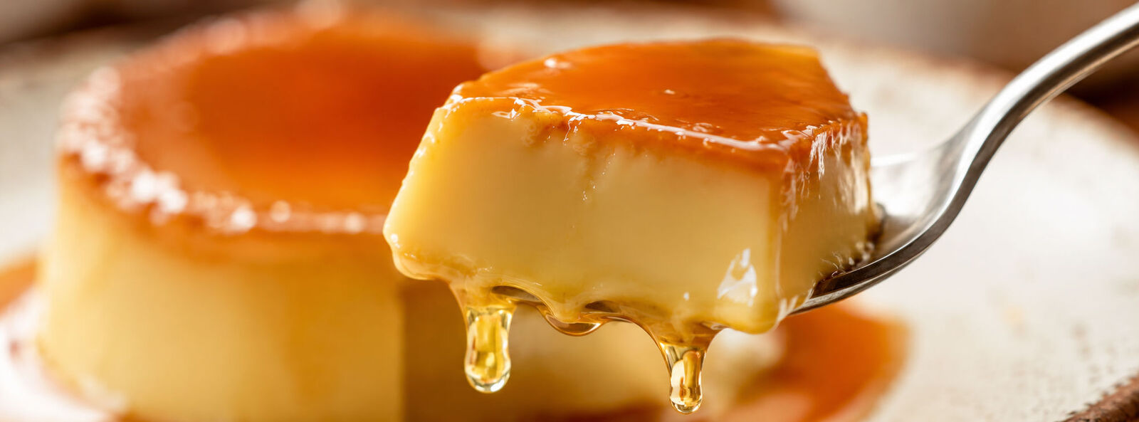 A close-up forkful of flan, showing its smooth custard texture and caramel drip