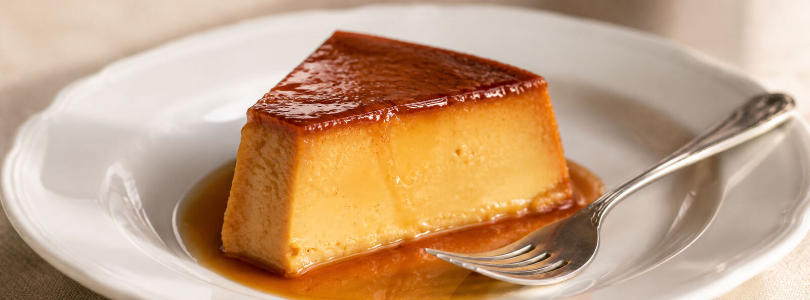 A slice of flan on a plate, showing the custard layers and caramel sauce