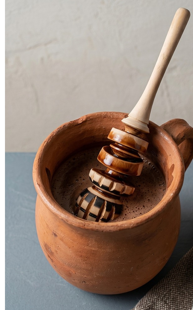 A molinillo submerged in a clay mug of hot chocolate, head fully in the liquid