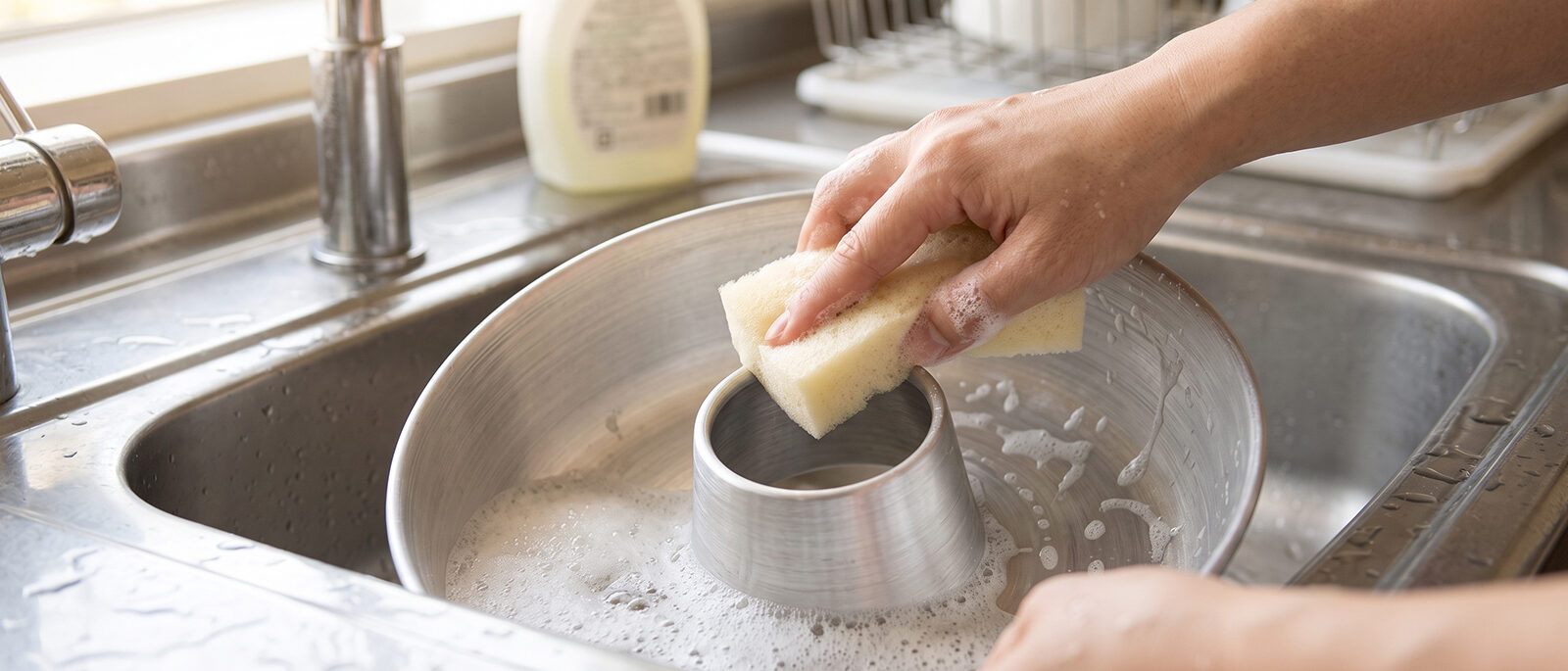 Hand washing an aluminum ring cake pan with a sponge in the sink